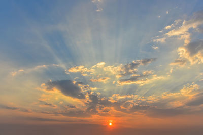 Low angle view of sunlight streaming through clouds during sunset