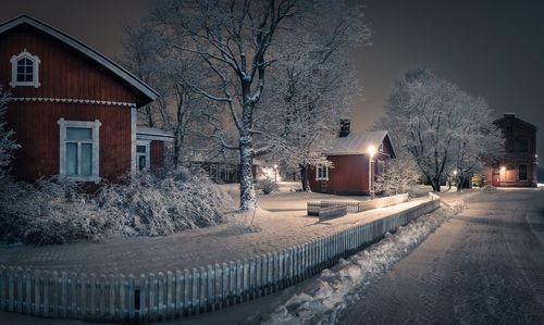 Snow covered road by buildings at night