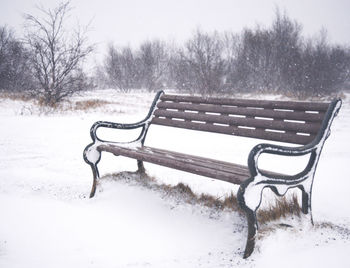 Empty bench on snow covered field against sky