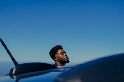 Man by car against blue sky
