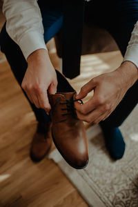 Low section of man holding shoes on wooden floor