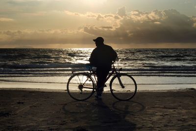 Rear view of man standing at beach against sky during sunset