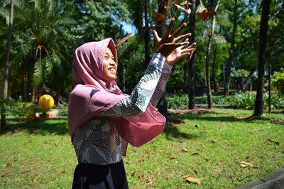Cheerful young woman playing with dry leaves at park