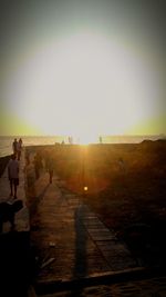 People walking on footpath against sky during sunset