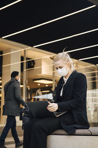 Businesswoman with face mask sitting with laptop outdoors