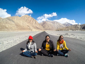 Full length of women sitting on country road against mountains during sunny day