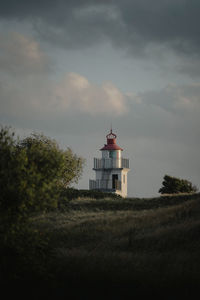 Lighthouse on field by building against sky