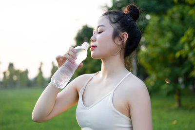 Side view of young woman drinking water in park