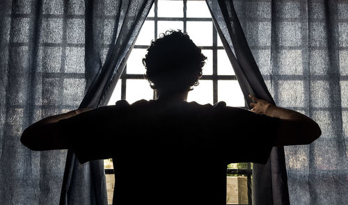 Rear view of man standing against window