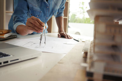 Midsection of female architect using drawing compass on blueprint at desk