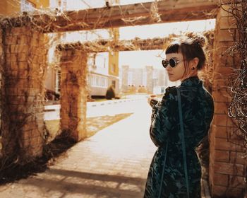 Portrait of young woman standing by built structure