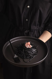 Woman holding a plate with spaghetti with cuttlefish ink and octopus