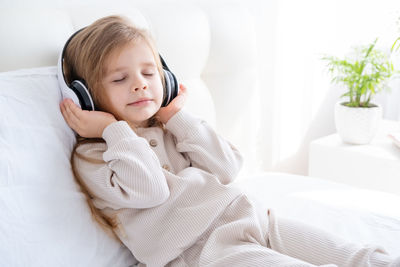 Cute girl listening music sitting on bed at home