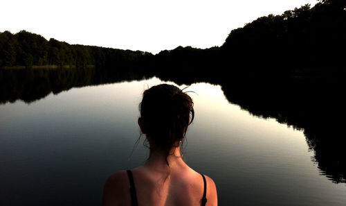 Rear view of woman standing by lake against clear sky
