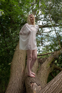 Full length of woman standing by tree trunk in forest