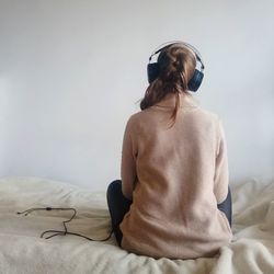 Rear view of woman listening music while sitting on bed at home