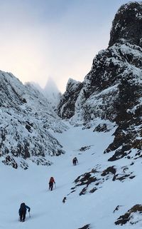 Low angle view of people climbing on snow covered mountain against sky