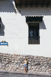 A young woman is standing near a white wall in cusco, peru