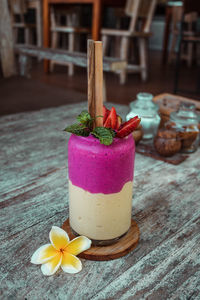 Smoothie in glass with straw, frangipani flower, sliced strawberry on wooden table. healthy dessert