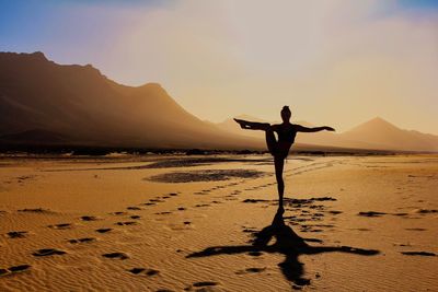 Man with arms raised on beach against sky during sunset