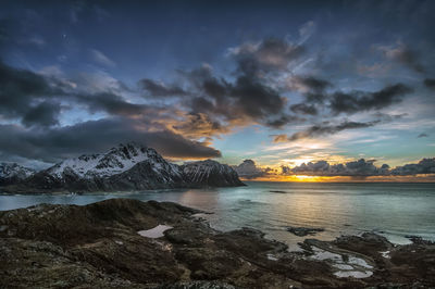 Scenic view of sea by mountains against sky during sunset