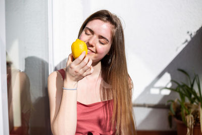 Smiling young woman holding lemon against wall