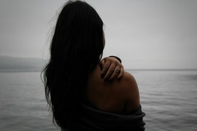 Rear view of woman touching shoulder by sea against sky