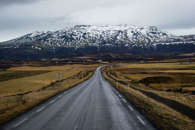 Road leading towards snowcapped mountains against sky