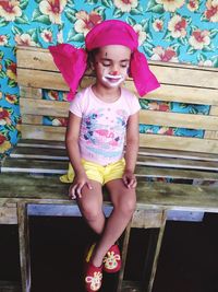 Full length of girl with face paint sitting on bench outdoors