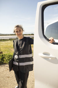 Portrait of smiling senior female engineer standing near van door at power station