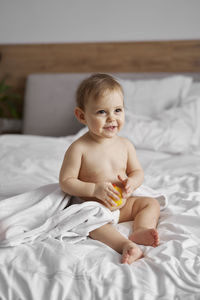 Cute baby boy sitting on bed at home