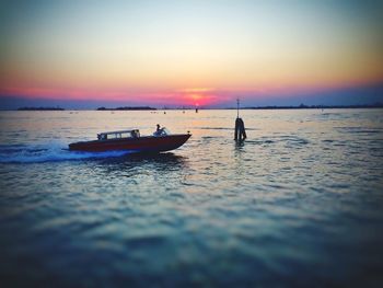 Man sailing in sea against sky during sunset