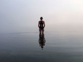 Rear view of woman in swimwear amidst sea during foggy weather