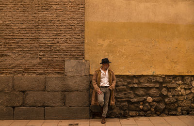 Full length of man in coat standing in front of yellow and brick wall during sand storm. madrid.