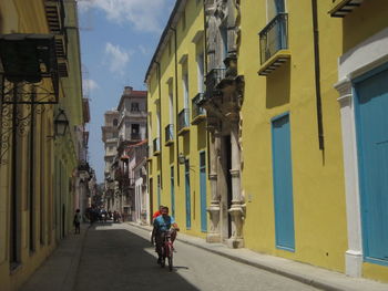 Rear view of man riding bicycle on street amidst buildings