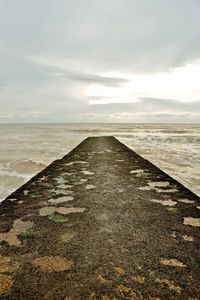 Empty road leading towards sea against sky