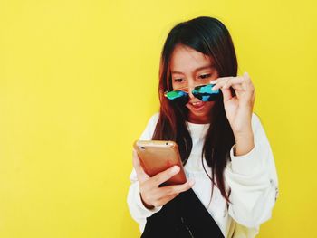 Portrait of young woman using smart phone against yellow background
