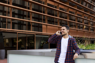 Man talking on phone while standing against building