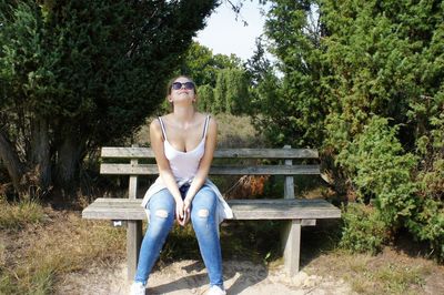 Full length of woman sitting on bench by trees