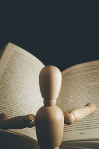 Close-up of wooden figurine reading book against black background