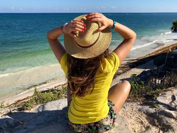 Woman wearing hat while sitting at beach against sky