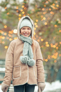 Portrait of young woman standing against illuminated christmas tree