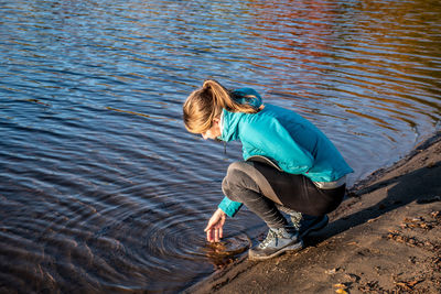 Full length of woman touching water while crouching during sunset