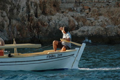 Man sitting on boat sailing in sea against mountain