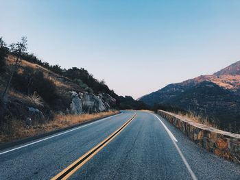 Empty road by mountains against clear sky