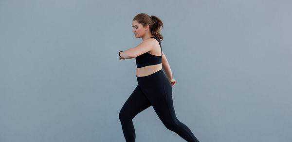 Side view of woman exercising against blue background