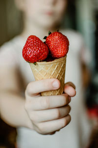 Child hand holding fresh organic strawberries in waffle ice cream cone. red berries in kid hand