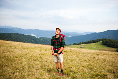 Smiling backpacker standing on mountain against sky