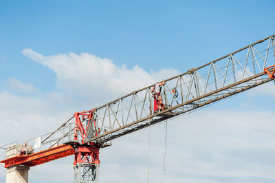 Low angle view of man standing crane against cloudy sky