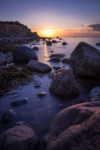 Rocks at sea shore against sky during sunset